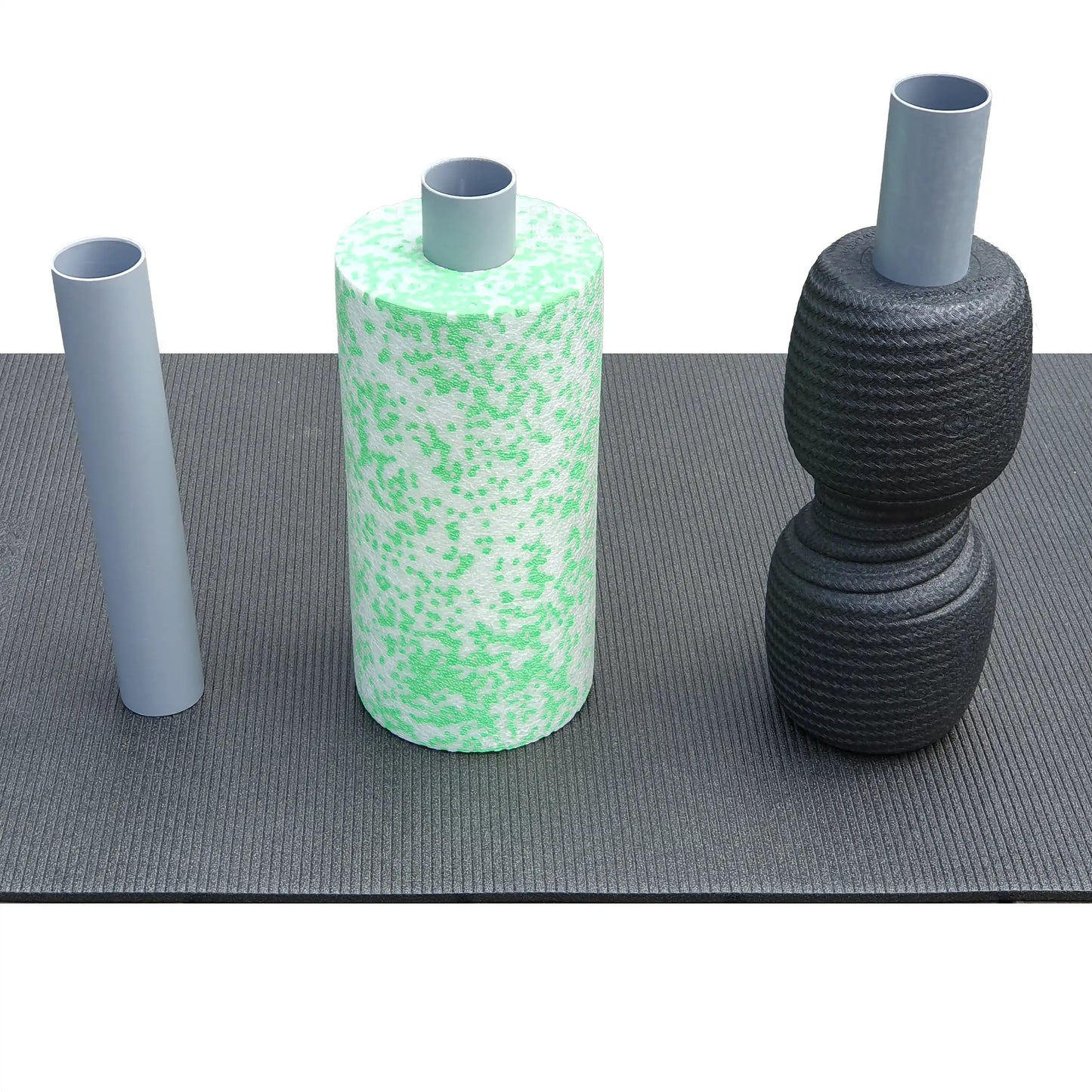 Uebersicht zur Zweitrollen-Vorbereitung: Links das einzelne DRYANGL Ersatz-Innenrohr, mittig eine Standard-Blackroll (Med) und rechts eine Blackroll Twin, jeweils mit eingeschobenem Stabilisierungsrohr auf einer Trainingsmatte.
